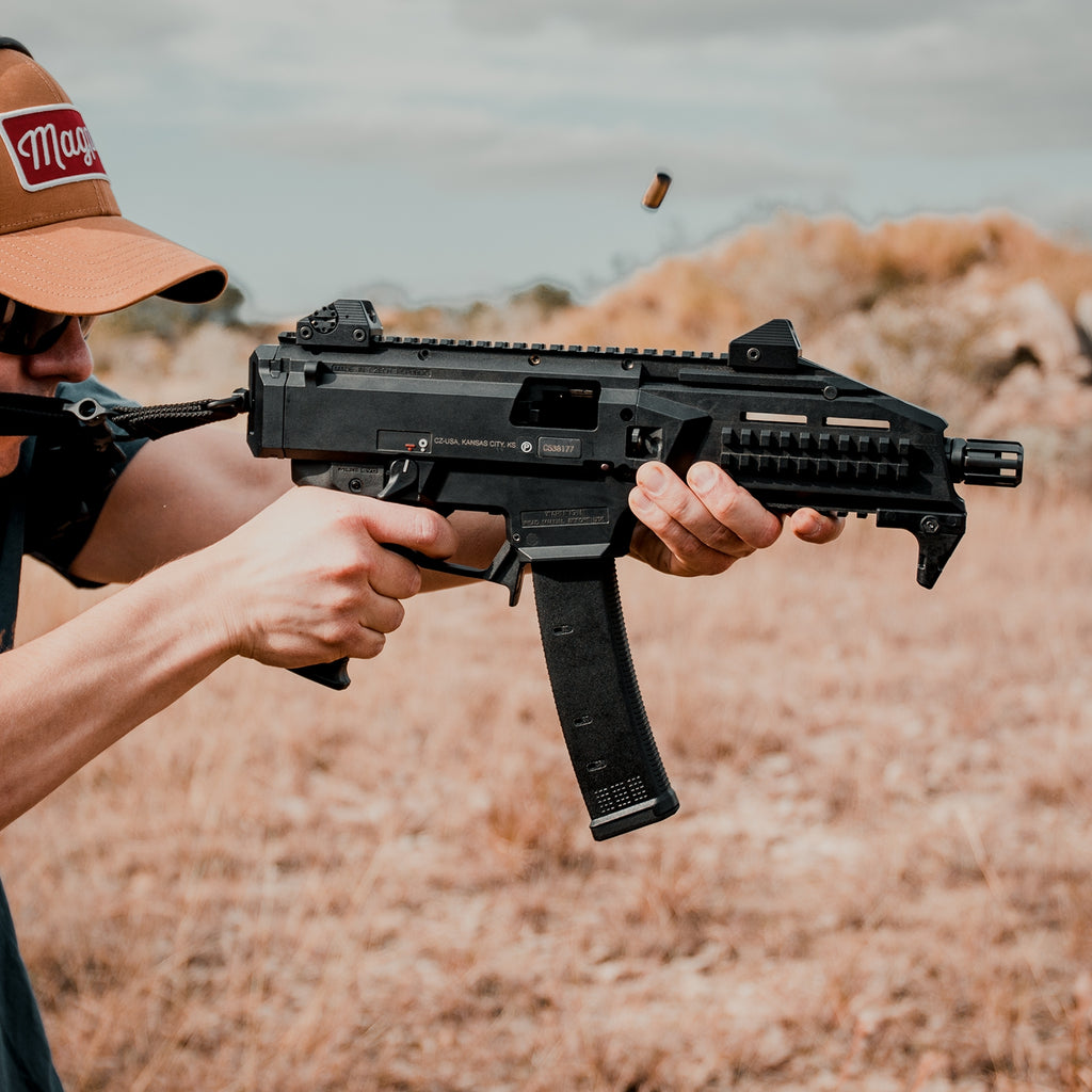 Person holding a black rifle in an outdoor setting with a blurred background