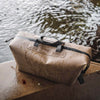 Wet duffel bag with black straps on a wooden surface near water