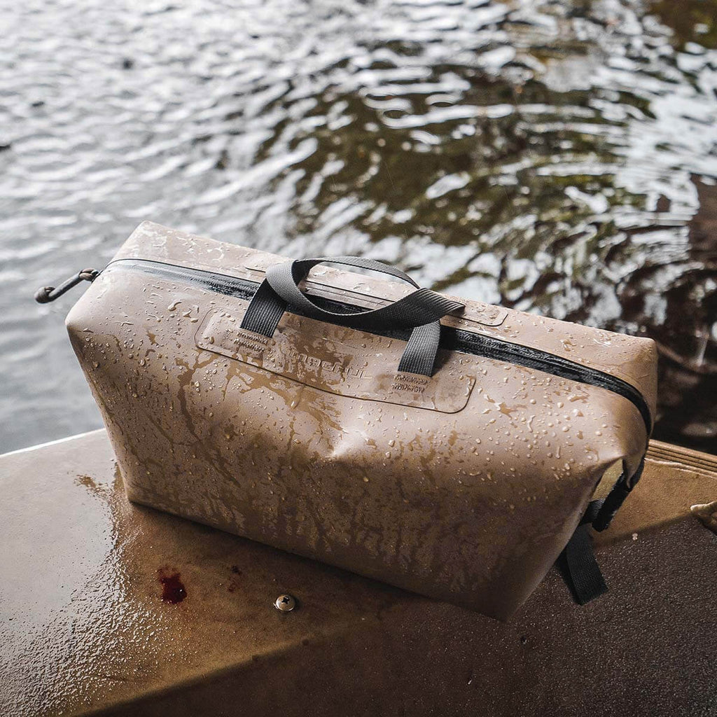 Wet duffel bag with black straps on a wooden surface near water
