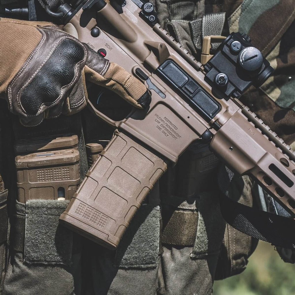 Close-up of a person holding a rifle with a magazine, wearing tactical gloves and gear.