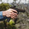 Hand holding a black handgun with a blurred natural background